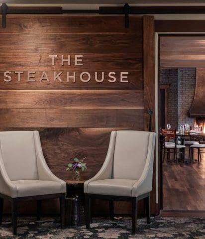 This image highlights the inviting entrance to The Steakhouse at Paso Robles Inn, offering guests a glimpse into its refined main dining room with soft lighting and a glowing fireplace. The setting combines rustic charm with modern elegance, perfect for those seeking Paso Robles Inn dining, wine country cuisine, or a romantic dinner in Paso Robles. The ambiance reflects the Inn’s dedication to local flavors, comfortable luxury, and exceptional service in the heart of Paso Robles wine country.