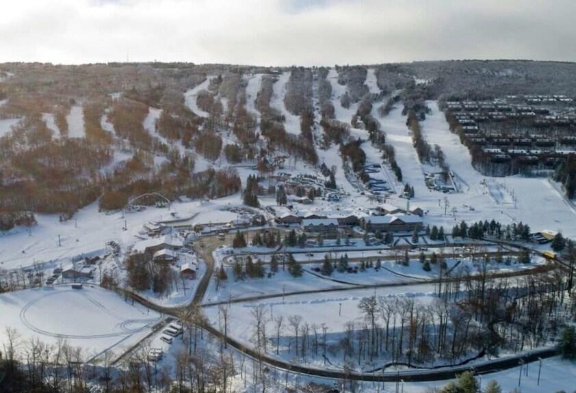 A breathtaking aerial view of Camelback Resort in Tannersville, Pennsylvania, showcasing the snow-covered slopes and trails of the popular Poconos ski resort. The image highlights Camelback snow park, a top PA ski destination known for its exciting ski and tubing experiences, perfect for family winter getaways and snow adventures in the Pocono Mountains.