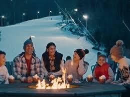 A joyful family enjoying hot cocoa around a cozy fire pit at a snowy mountain resort, capturing candid winter photography and memory documentation moments after a fun day of skiing and tubing in the Poconos.