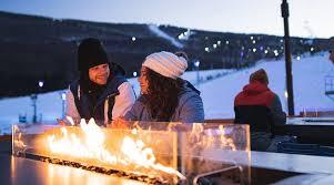 Guests enjoying a cozy evening by the firepit at Camelback Resort in the Poconos after a fun day of skiing and tubing. This scenic winter moment at the PA ski destination highlights the perfect winter getaway with breathtaking views of the slopes and relaxing snow park activities.