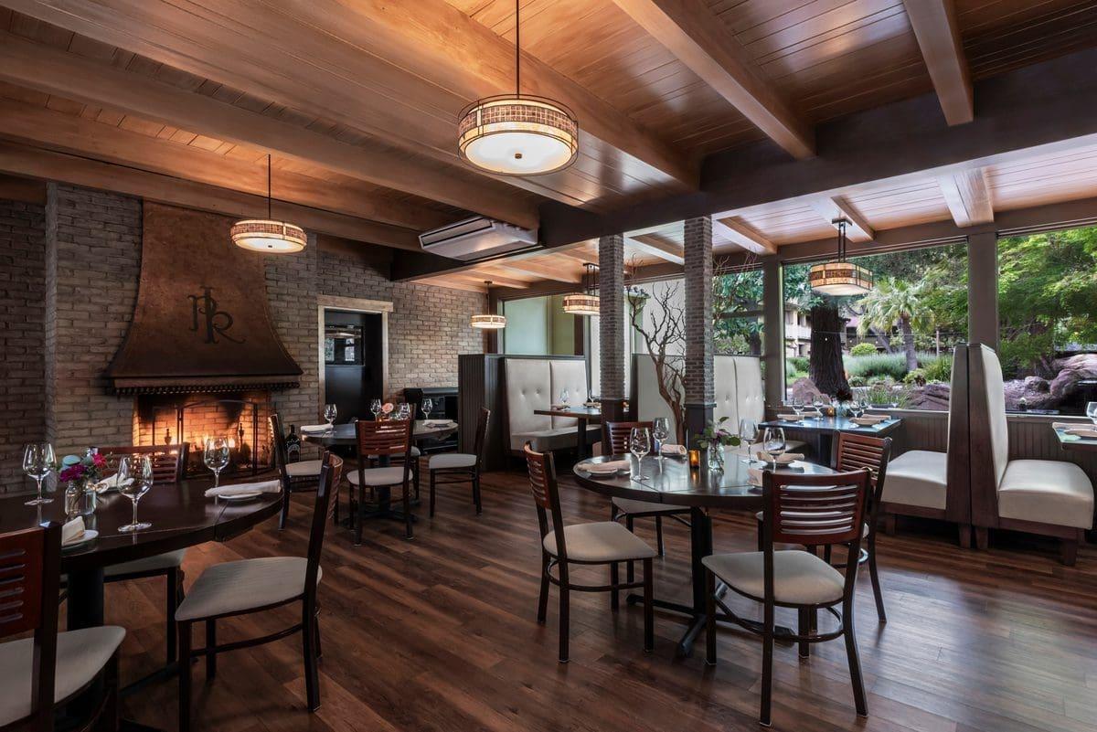 Cozy indoor dining room at Paso Robles Inn with a warm fireplace, elegant table settings, and views of the garden, showcasing fine dining in Paso Robles wine country.