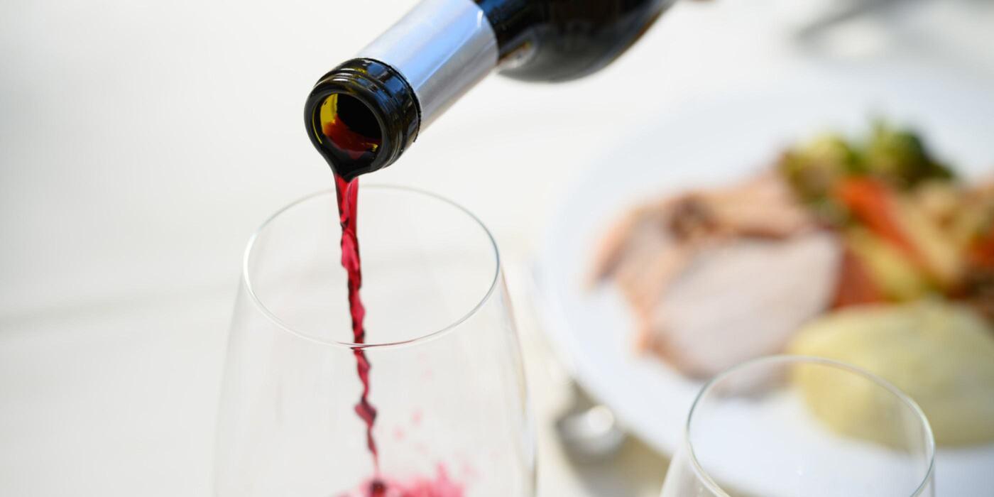 A close-up view of red wine being elegantly poured into a glass beside a gourmet meal, capturing the essence of refined indulgence in Napa Valley. Your refined wine country escape awaits among the vineyards, where every pour tells the story of relaxation and luxury.