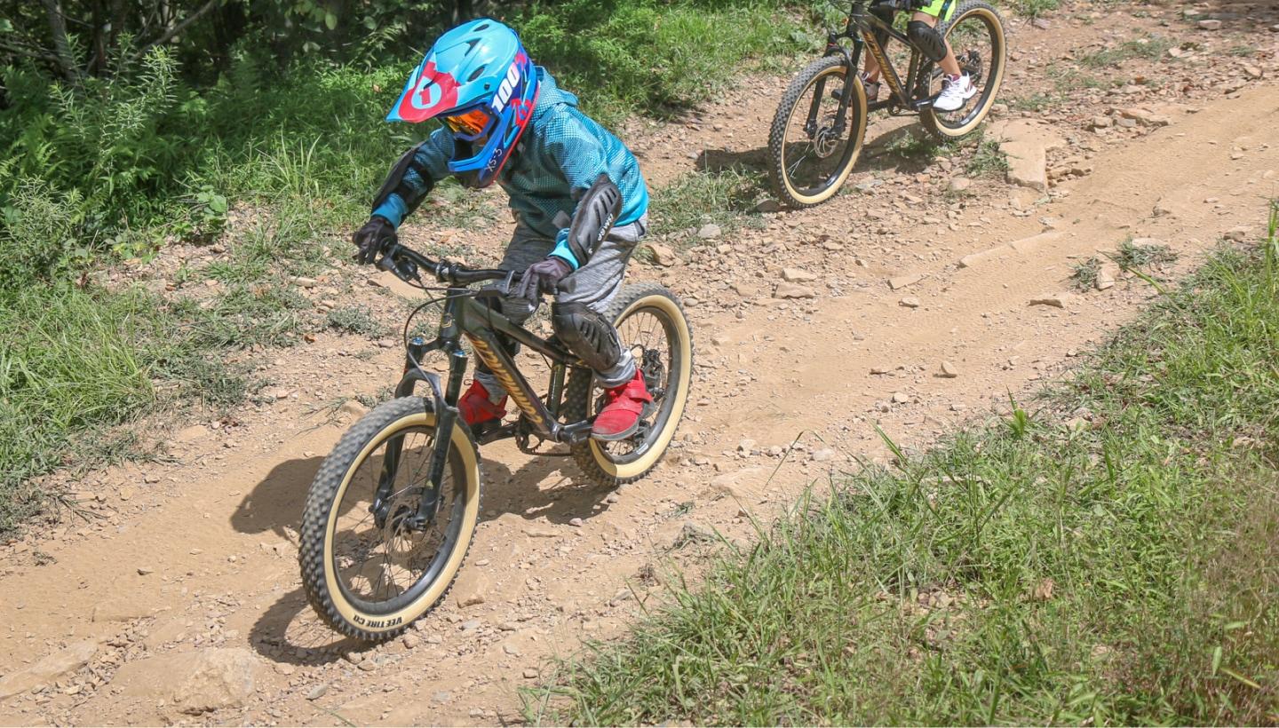 Young riders wearing helmets and protective gear biking down a dirt trail at Blue Mountain Bike Park, demonstrating proper safety requirements and trail etiquette.