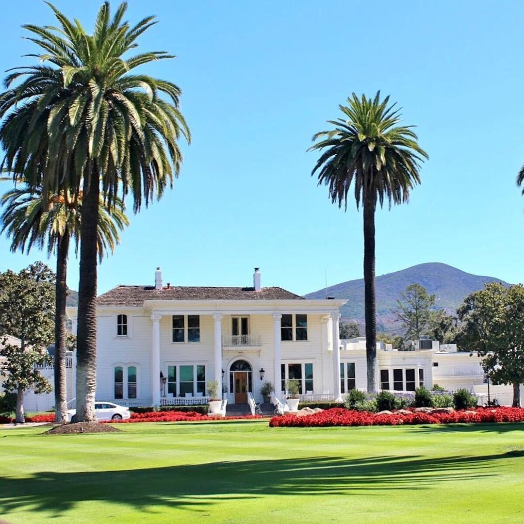 Where vineyard dreams meet luxury living in California Wine Country – this stunning image showcases the iconic Mansion at Silverado Resort in Napa Valley. Framed by tall palm trees, lush green lawns, and vibrant flower beds, the resort's historic architecture stands as a timeless symbol of elegance and tranquility. Perfectly blending classic charm with modern sophistication, Silverado Resort invites guests to experience the beauty, relaxation, and indulgence that define a true Napa Valley escape.