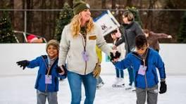 A smiling woman holds hands with two young children as they enjoy ice skating at Massanutten Resort’s outdoor rink, showing that beginners can learn ice skating easily and safely at the resort.