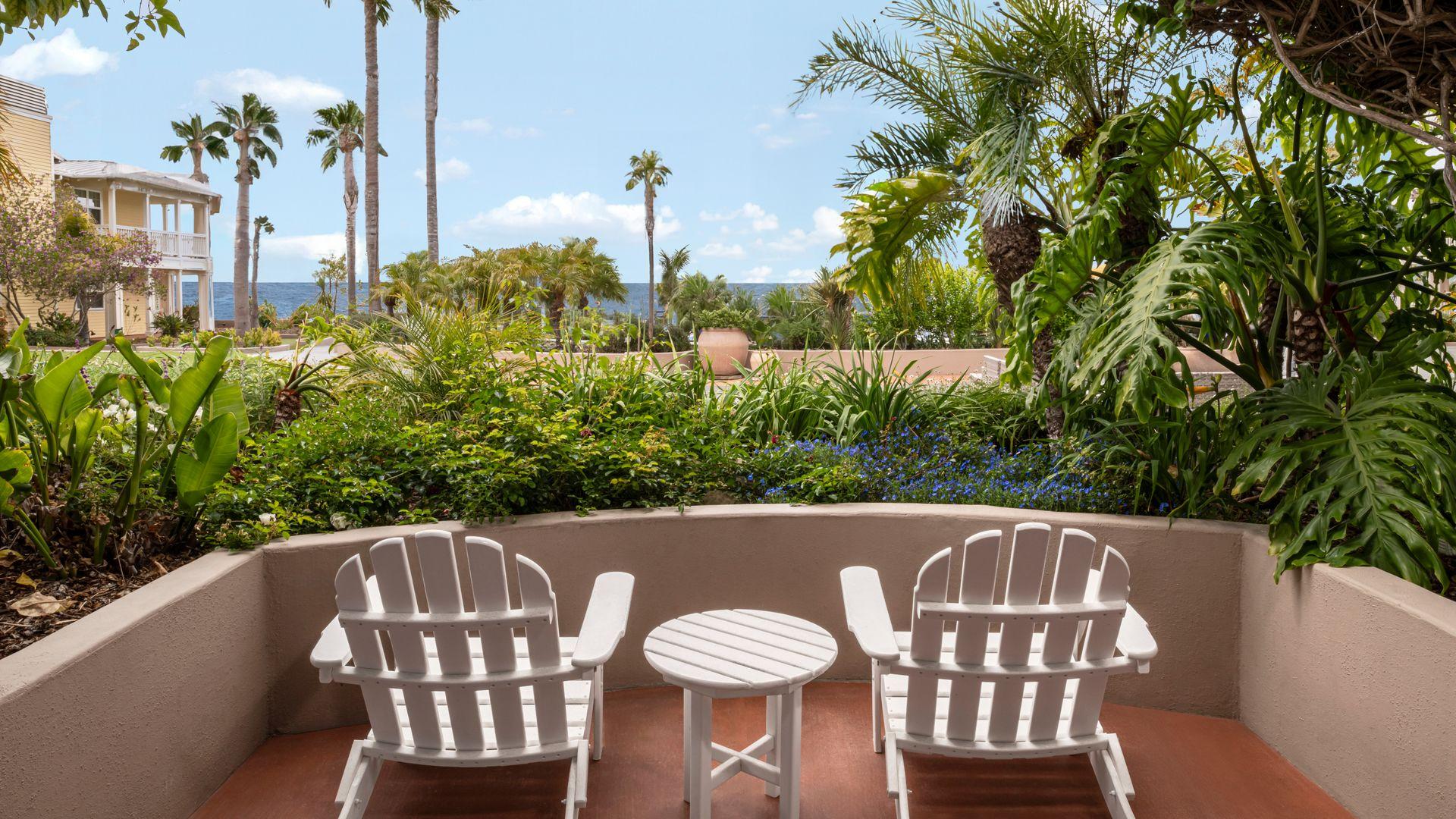 Peaceful garden-view patio with two white chairs overlooking lush greenery and the ocean at Avila Lighthouse Suites — seasonal offers and exclusive packages you can't miss for a perfect coastal escape.