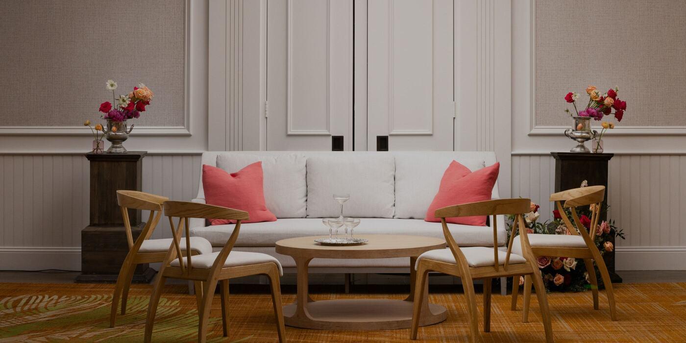 A beautifully designed sitting area featuring a white sofa accented with coral pillows, surrounded by elegant wooden chairs and fresh floral arrangements, embodying the warmth and sophistication of personalized accommodations for every traveler’s needs at Silverado Resort in Napa Valley.