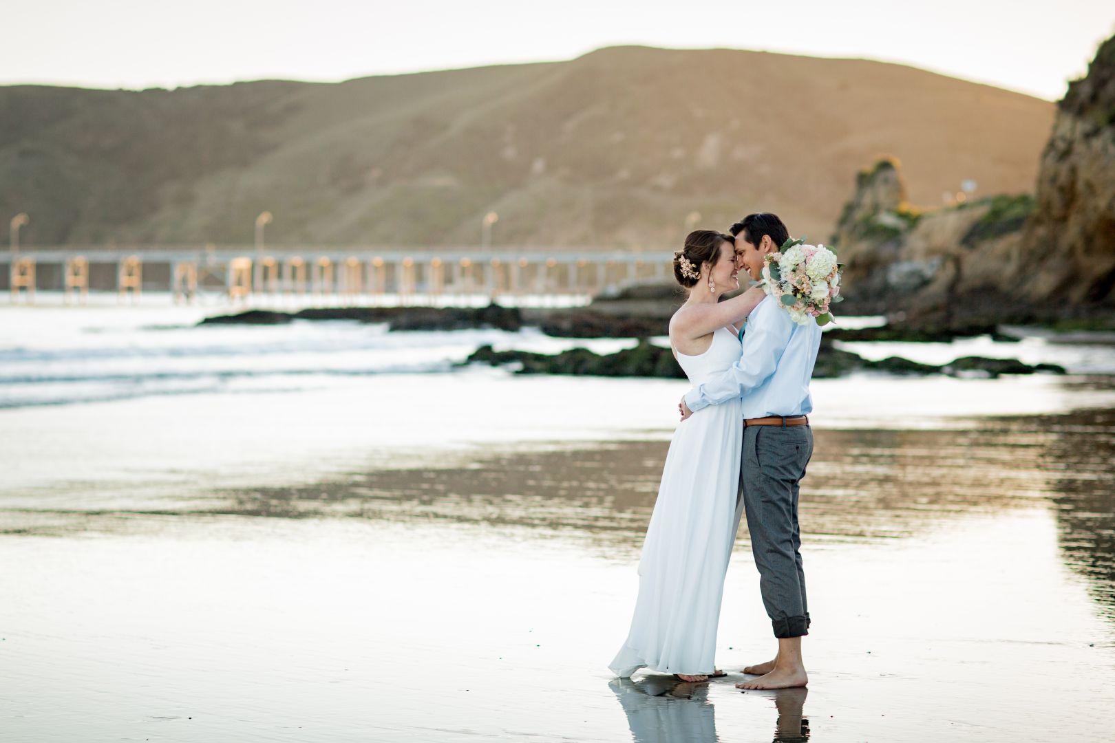 Romantic couple embracing on the beach at Avila Lighthouse Suites, celebrating love with ocean waves and golden hills in the background — featured vacation packages and exclusive beach hotel offers for couples seeking luxury and romance.